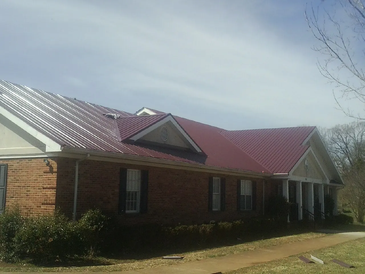 Red metal roof with gabled entries on a long brick building, from a Hail Damage Roof Repair job in Darrington