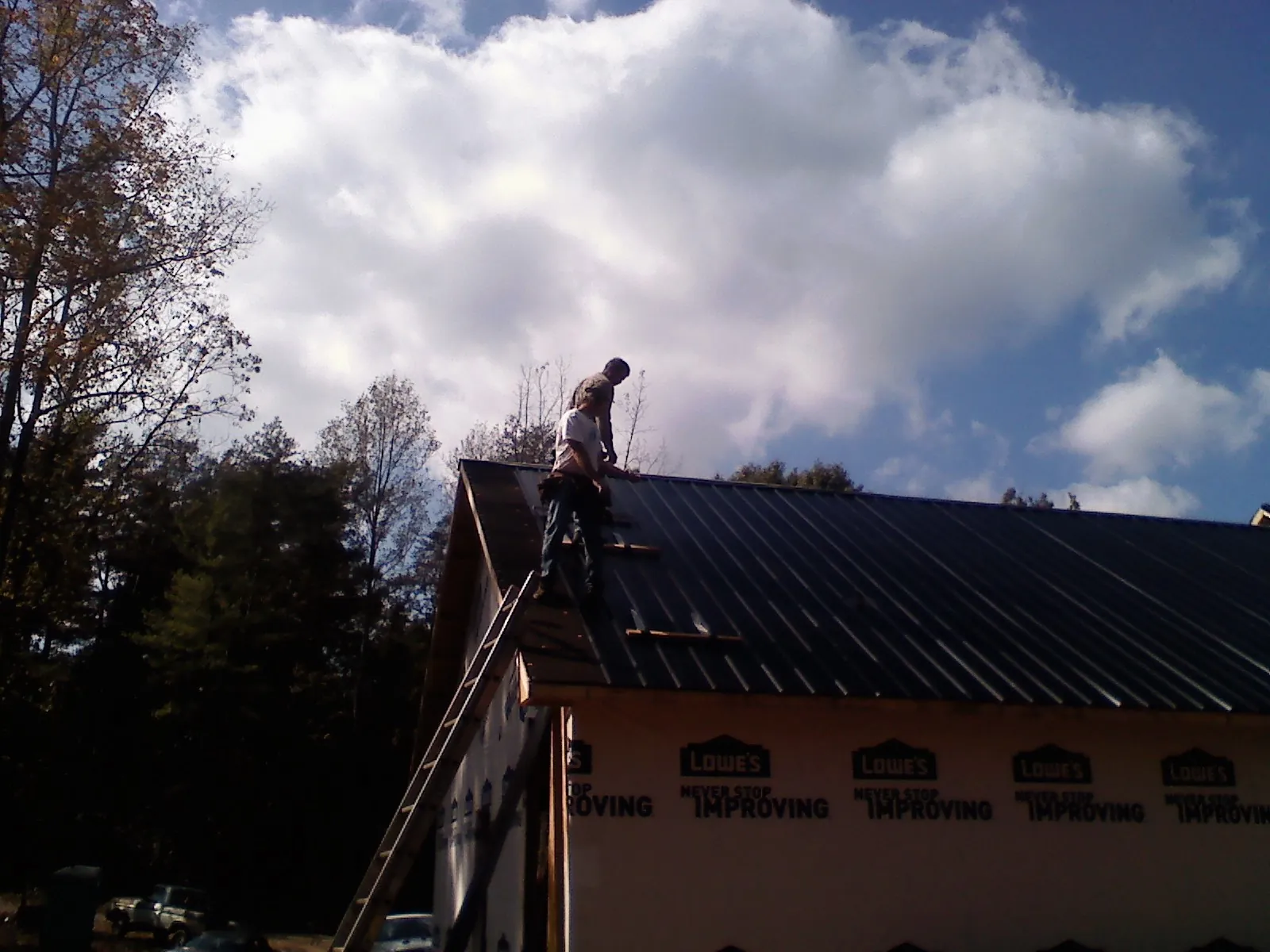 Roofer fastening dark metal panels high against a cloudy sky, from a Roof Inspection job in Darrington