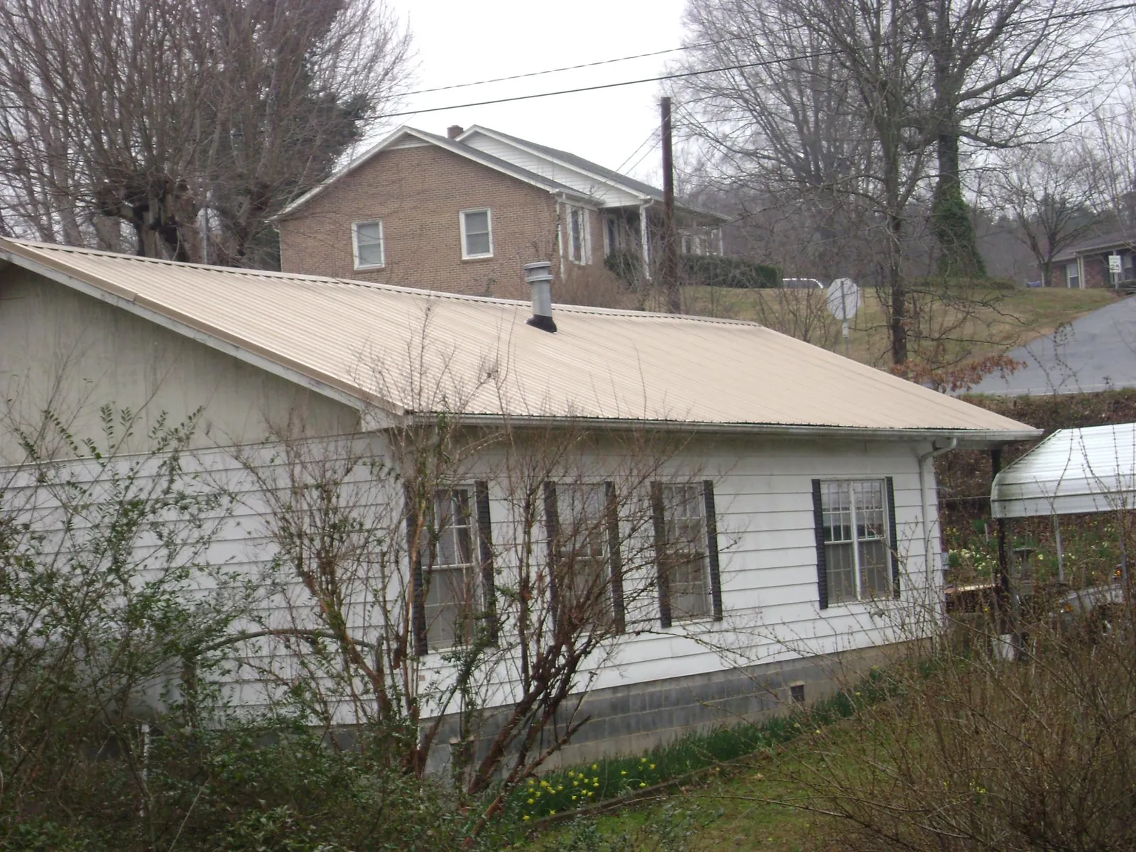 Tan metal roof on a white sided house set into a hillside — Commercial Roofing by Roofing Brothers in Darrington